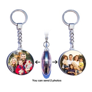 May include: A silver keyring with two round photo inserts. The keyring has a silver chain and a silver ring. The photo inserts are both round and have a silver border. The photo inserts show two different photos of families. The text "You can send 2 photos" is printed below the keyrings.