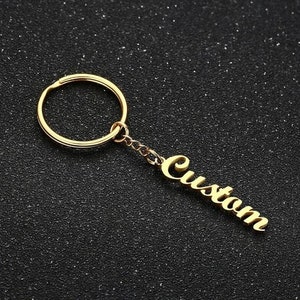 May include: Gold-toned keychain with a round ring and a dangling charm that says "Custom" in a cursive font.