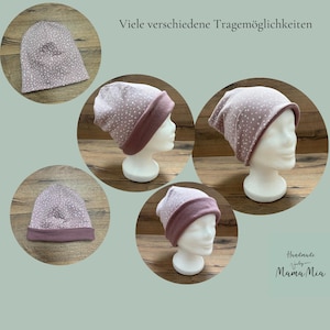 May include: A mauve beanie with a white speckled pattern, shown in multiple configurations on white mannequin heads. The hat features a solid mauve folded brim and a speckled crown. The text "Viele verschiedene Tragem&ouml;glichkeiten" and "Handmade by Mama Mia" are visible.