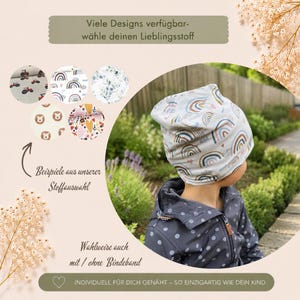 May include: A beanie hat with a rainbow pattern worn on a head, accompanied by five circular fabric swatches featuring tractors, rainbows, leaves, lions, and hearts. Text includes 'Viele Designs verf&uuml;gbar-w&auml;hle deinen Lieblingsstoff', 'Beispiele aus unserer Stoffauswahl', 'Wahlweise auch mit / ohne Bindeband', and 'INDIVIDUELL F&Uuml;R DICH GEN&Auml;HT &ndash; SO EINZIGARTIG WIE DEIN KIND'.