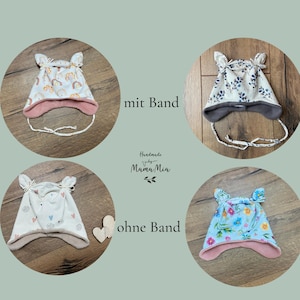 K&ouml;nnte beinhalten: Vier Baby-M&uuml;tzen mit &ouml;hrchenartigen Ecken. Zwei M&uuml;tzen haben Bindeb&auml;nder mit der Beschriftung mit Band, zwei M&uuml;tzen ohne B&auml;nder sind mit ohne Band beschriftet. Die Muster zeigen Regenb&ouml;gen, blaue Bl&auml;tter, Herzen und bunte Blumen.