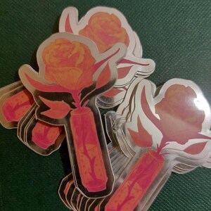 Op de afbeelding: Een stapel rozen stickers met een gouden folie afwerking. De rozen zijn oranje en roze met groene stelen en bladeren.