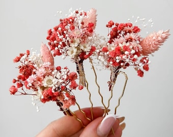 May include: Set of four gold hair pins adorned with dried flowers in shades of pink and white. The flowers are arranged in a cluster and secured to the pins with wire.
