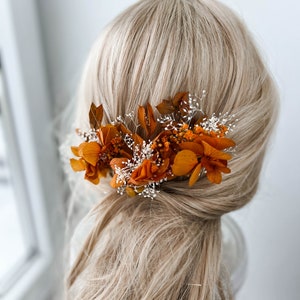 May include: A hair comb with dried orange and white flowers. The comb is worn in a woman's hair.