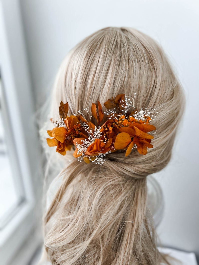 May include: A hair comb with dried orange and white flowers. The comb is worn in a woman's hair.