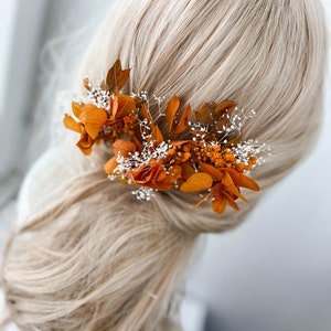 May include: A hair accessory with dried orange flowers and white baby's breath. The flowers are arranged in a cluster and are attached to a hair clip.