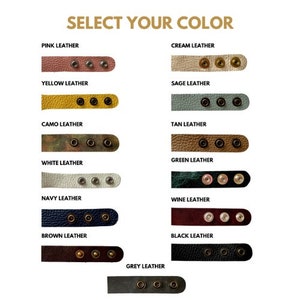Puede incluir: Una selecci&oacute;n de correas de cuero en varios colores, incluyendo rosa, crema, amarillo, salvia, camuflaje, marr&oacute;n, verde, blanco, azul marino, vino, marr&oacute;n, gris y negro. Cada correa tiene tres remaches de metal dorado.