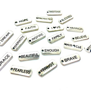 Puede incluir: Una colecci&oacute;n de dijes de plata con varias palabras y frases inspiradoras, que incluyen "Dream", "Grace", "Namaste", "Hope", "Protected", "Faith", "Imagine", "Blessed", "Love", "Inspire", "Warrior", "Family", "Believe", "Beautiful", "Enough", "Miracle", "Brave", "Fearless", "Trust" y "Forever".