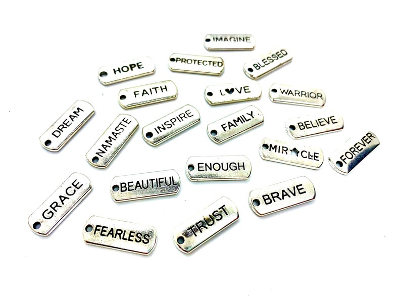 Puede incluir: Una colecci&oacute;n de dijes de plata con varias palabras y frases inspiradoras, que incluyen "Dream", "Grace", "Namaste", "Hope", "Protected", "Faith", "Imagine", "Blessed", "Love", "Inspire", "Warrior", "Family", "Believe", "Beautiful", "Enough", "Miracle", "Brave", "Fearless", "Trust" y "Forever".