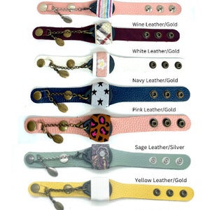 Puede incluir: Una colecci&oacute;n de pulseras de cuero con diferentes correas de cuero de colores y dijes. Las pulseras tienen acentos plateados y dorados y est&aacute;n decoradas con varios patrones y dise&ntilde;os. Las pulseras est&aacute;n dispuestas verticalmente en una fila, con el texto "Wine Leather/Silver", "White Leather/Silver", "Navy Leather/Silver", "Pink Leather/Silver", "Wine Leather/Gold", "White Leather/Gold", "Navy Leather/Gold", "Pink Leather/Gold", "Sage Leather/Silver", "Yellow Leather/Gold", "Sage Leather/Gold", "Yellow Leather/Silver" y "Camo Leather/Gold" escrito debajo de cada pulsera.