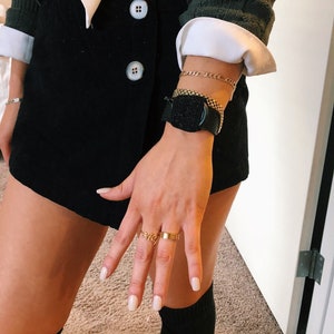 Puede incluir: Una persona que lleva una falda negra, una camisa blanca y un reloj negro con una pulsera de cadena dorada. La persona tambi&eacute;n lleva un anillo de oro con la palabra "love" en &eacute;l.