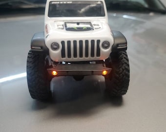 May include: White toy Jeep Wrangler with black tires and orange lights. The Jeep has a black grill and a black hood with a black air intake. The Jeep is sitting on a gray surface.