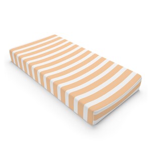 May include: A peach-colored and white striped fitted crib sheet. The sheet is made of soft, breathable fabric and is perfect for a baby's nursery.