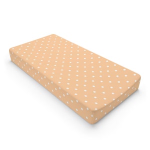 May include: A peach-colored fitted crib sheet with a white polka dot pattern.