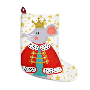 May include: A white Christmas stocking with a gray mouse wearing a red and gold king's outfit. The stocking is decorated with gold stars.