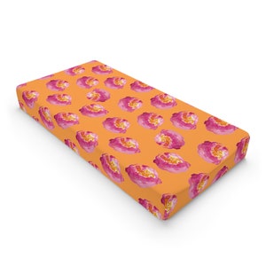 May include: Orange fitted crib sheet with a pink floral pattern.
