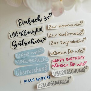 May include: A collection of various sticker labels with handwritten text in black, brown, and pink. The labels include phrases like "Einfach so", "Gutschein", "Happy Birthday", and "&Uuml;berraschung". Each label has a heart symbol.