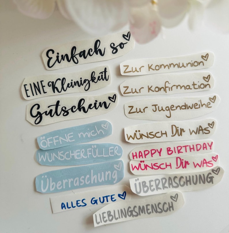 May include: A collection of various sticker labels with handwritten text in black, brown, and pink. The labels include phrases like "Einfach so", "Gutschein", "Happy Birthday", and "&Uuml;berraschung". Each label has a heart symbol.