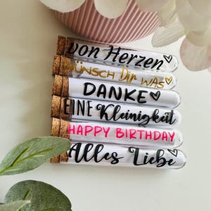 May include: A collection of glass tubes with cork stoppers, each labeled with a different message in black or gold script. The messages include "Von Herzen", "Wunsch Dir Was", "Danke", "Eine Kleinigkeit", "Happy Birthday", and "Alles Liebe".