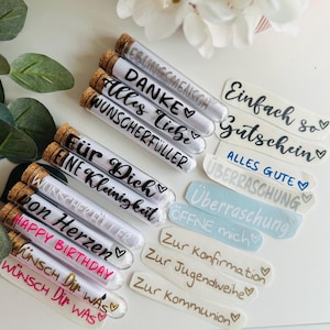 May include: A collection of glass tubes with cork stoppers, each containing a rolled-up message. The tubes have various phrases written on them in black and white, such as "Happy Birthday" and "W&uuml;nsch Dir Was". Also included are stickers with phrases.