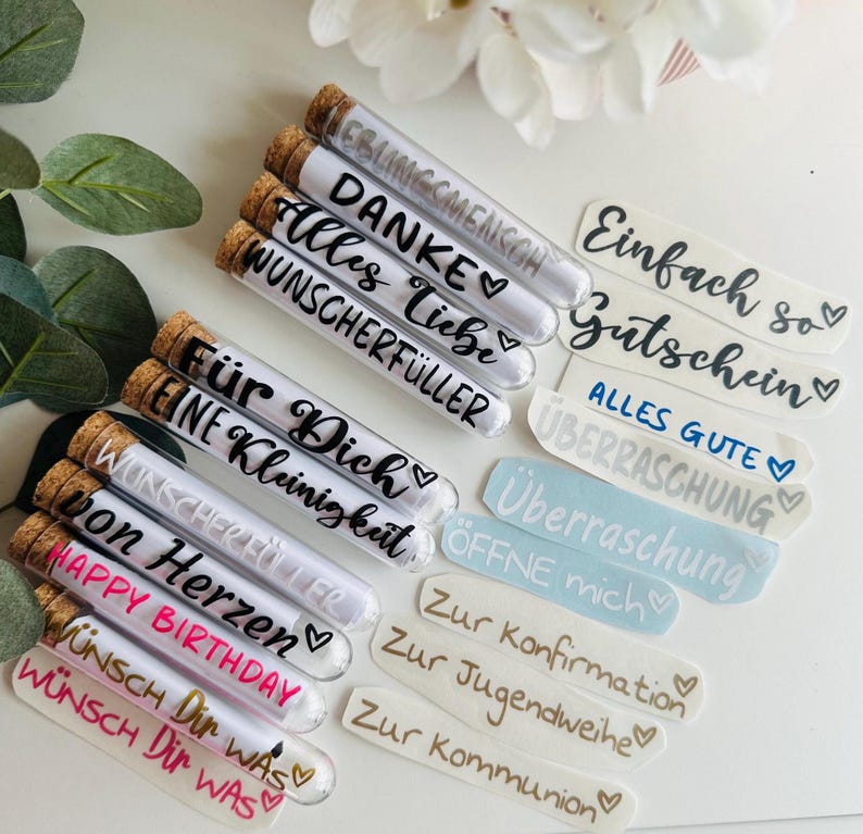 May include: A collection of glass tubes with cork stoppers, each containing a rolled-up message. The tubes have various phrases written on them in black and white, such as "Happy Birthday" and "W&uuml;nsch Dir Was". Also included are stickers with phrases.