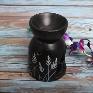 May include: Black ceramic oil burner with a floral design. The burner has a small bowl on top for holding oil and a space below for a tea light.
