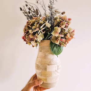 May include: A wooden vase with a unique, geometric design, holding a bouquet of dried hydrangeas and other dried flowers.