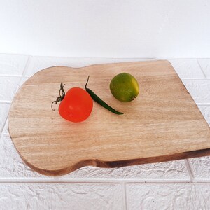 May include: A wooden cutting board with a unique shape, featuring a green chili pepper, a red tomato, and a green lime.