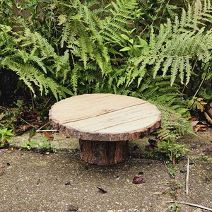 Puede incluir: Un soporte para tartas de madera r&uacute;stico con un borde de corteza natural y una base de tronco de &aacute;rbol. El soporte est&aacute; hecho de madera y tiene un acabado natural. Es perfecto para exhibir tartas, cupcakes u otros postres.
