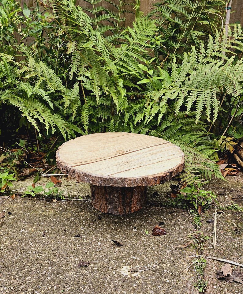 Puede incluir: Un soporte para tartas de madera r&uacute;stico con un borde de corteza natural y una base de tronco de &aacute;rbol. El soporte est&aacute; hecho de madera y tiene un acabado natural. Es perfecto para exhibir tartas, cupcakes u otros postres.
