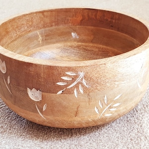May include: A wooden bowl with a carved floral design. The bowl is light brown with white floral carvings.