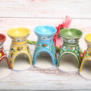 May include: Four ceramic oil burner diffusers in different colors: brown, yellow, blue, and green. Each diffuser has a floral design and a hole in the center for a tea light.