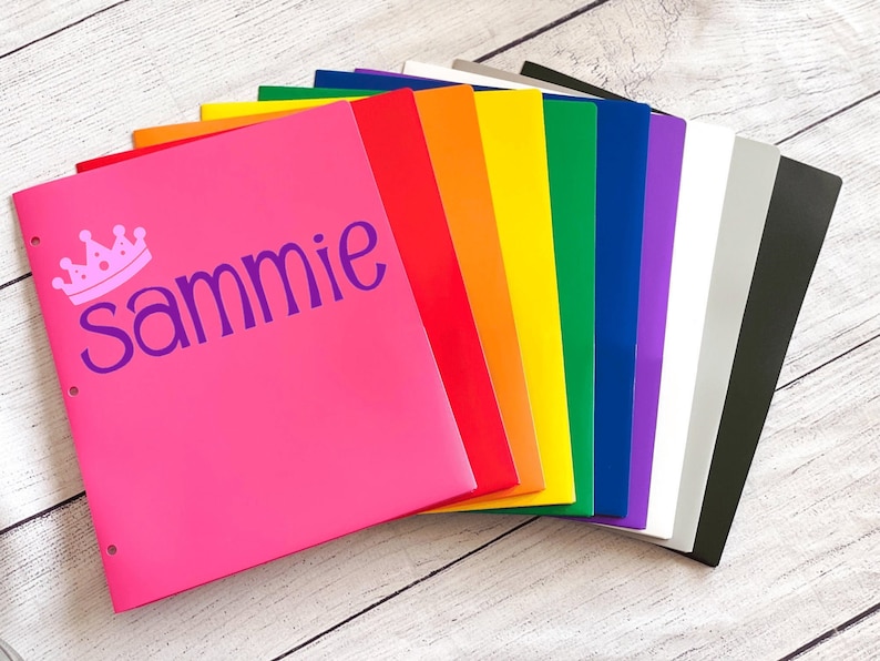 May include: A stack of colorful plastic folders with a pink folder on top that has a crown and the name "sammie" on it.