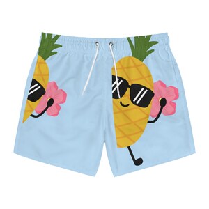 May include: Light blue swim trunks with a cartoon pineapple wearing sunglasses and holding a pink flower. The pineapple is yellow with a brown stem and green leaves.