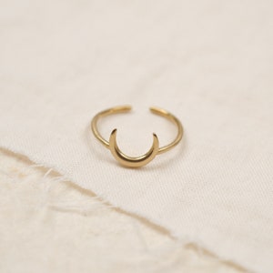 Könnte beinhalten: Ein goldener Halbmondring. Der Ring ist schlicht und zart, mit einer glatten Oberfläche.