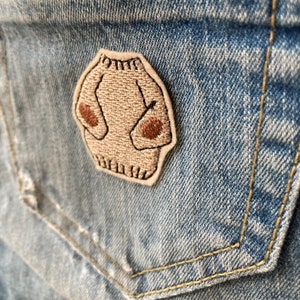 Op de afbeelding: Een bruin geborduurd trui-patch met een bruine omtrek, genaaid op een blauw denim jack.