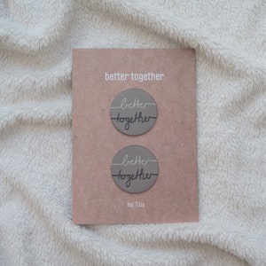 Könnte beinhalten: Zwei runde graue Papiersticker mit dem Text "better together" in weiß und schwarz auf jedem Sticker. Die Sticker befinden sich auf einer braunen Karte mit dem Text "better together" und "hej Tilly" in schwarz.