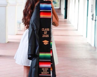 May include: A black graduation stole featuring horizontal stripes in vibrant colors including red, blue, green, and yellow. The text "CLASS OF 2025" is printed in gold above a graduation cap icon, with "SAN DIEGO STATE UNIVERSITY" printed below.