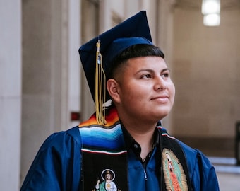 May include: A person wearing a blue graduation gown and cap, with a colorful stole featuring religious imagery. The stole has the text "CLASS OF 2024" on it.