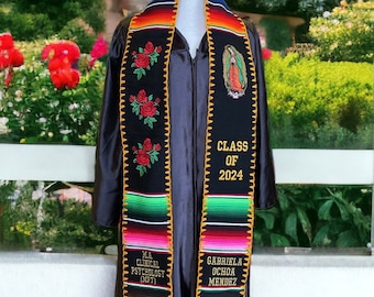 May include: Black graduation stole with colorful stripes and embroidered roses, a religious image, and the text "CLASS OF 2024". The stole also has the text "M.A. CLINICAL PSYCHOLOGY (MFT)" and "GABRIELA OCHOA MENDEZ".