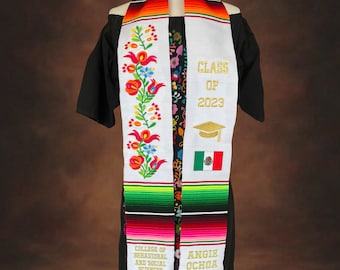 May include: White graduation stole with colorful embroidery and the text "Class of 2023" in gold. The stole also features the text "College of Behavioral and Social Sciences" and "Angie Ochoa".