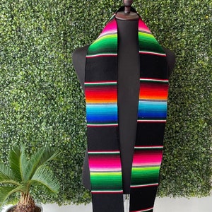 May include: A black graduation stole with colorful stripes in red, orange, yellow, green, blue, and pink. The stole is displayed on a mannequin against a green backdrop.