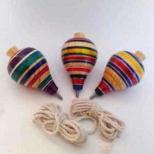 May include: Three colourful wooden spinning tops with a white string. The tops are decorated with stripes of red, yellow, blue, green, and purple.