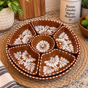 May include: A circular terracotta serving set featuring a central round bowl surrounded by five wedge-shaped dishes. Each piece is decorated with white hand-painted floral patterns and a dotted border. Small square labels are attached to each dish.