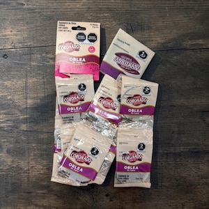 May include: A collection of Coroando Oblea de Cajeta wafer sandwich snacks in individual beige and purple packaging. The items include one rectangular cardboard display box and several smaller, sealed plastic pouches featuring the brand logo.
