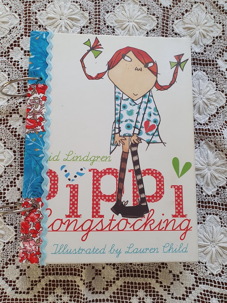 May include: A white book with a red and blue patterned cover. The cover features a cartoon illustration of a girl with red hair and a blue dress. The title of the book is "Pippi Longstocking" and the author is "Astrid Lindgren". The book is illustrated by Lauren Child.