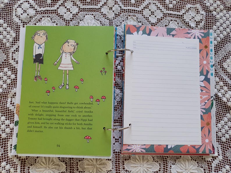 May include: An open book with a green cover and illustrations of two children. The book is open to a page with text about a field and a dagger. The opposite page is blank and has a floral design.