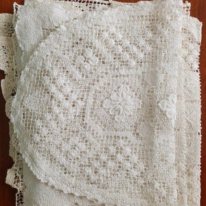 Puede incluir: Un conjunto de tapetes y manteles individuales bordados en blanco roto. Los delicados diseños florales y el tejido abierto crean una estética vintage y artesanal. Los artículos están hechos de una tela suave y texturizada.