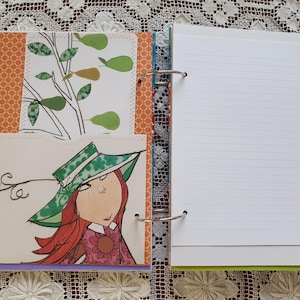 May include: A colorful binder with a white page open, showing lined paper. The binder has a green, blue, and orange design. The page has handwritten text on the right side.