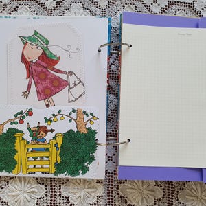 May include: A white binder with a purple cover and a white page with a grid pattern. The binder has a ring mechanism and a decorative floral pattern on the spine. The page has the text "Things I Love" at the top.